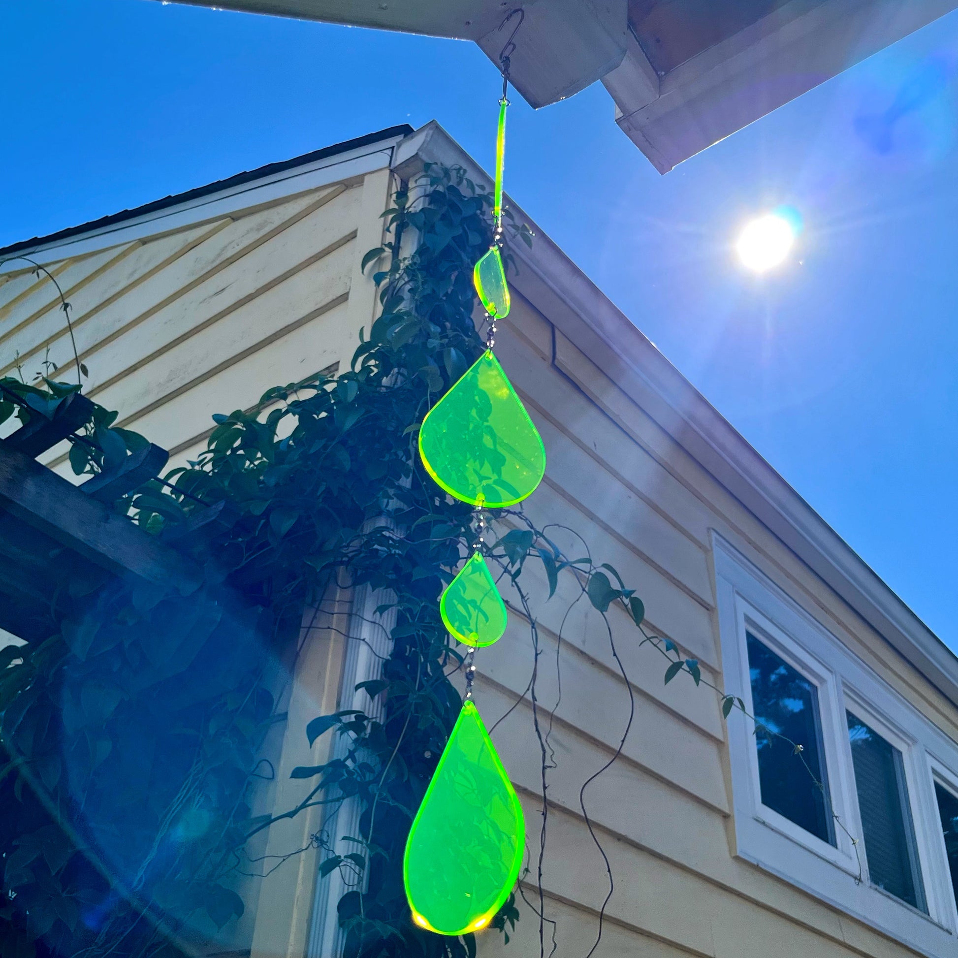 A green fluorescent suncatcher hanging from the eaves of a building, catching the sun’s rays in front of a blue sky.
