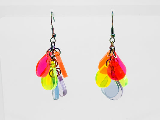 Colorful acrylic dangle earrings displayed on a clear acrylic stand, featuring neon pink, orange, yellow, blue and purple translucent shapes against a white background.