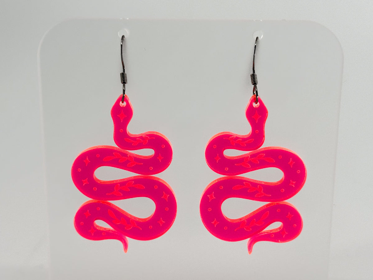 A pair of fluorescent pink snake-shaped dangle earrings with silver fishhook wires, displayed on a clear acrylic stand against a light gray background.