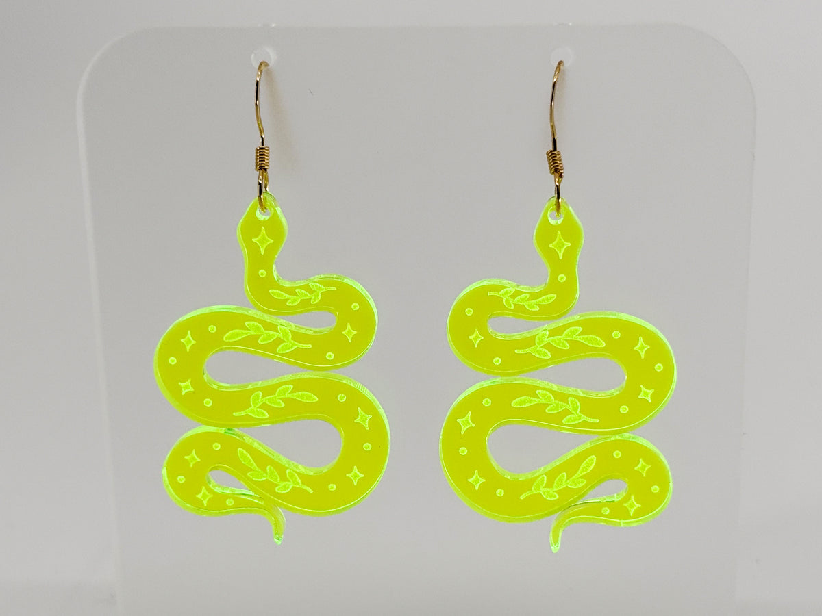 A pair of fluorescent green snake-shaped dangle earrings with gold fishhook wires, displayed on a clear acrylic stand against a light gray background.