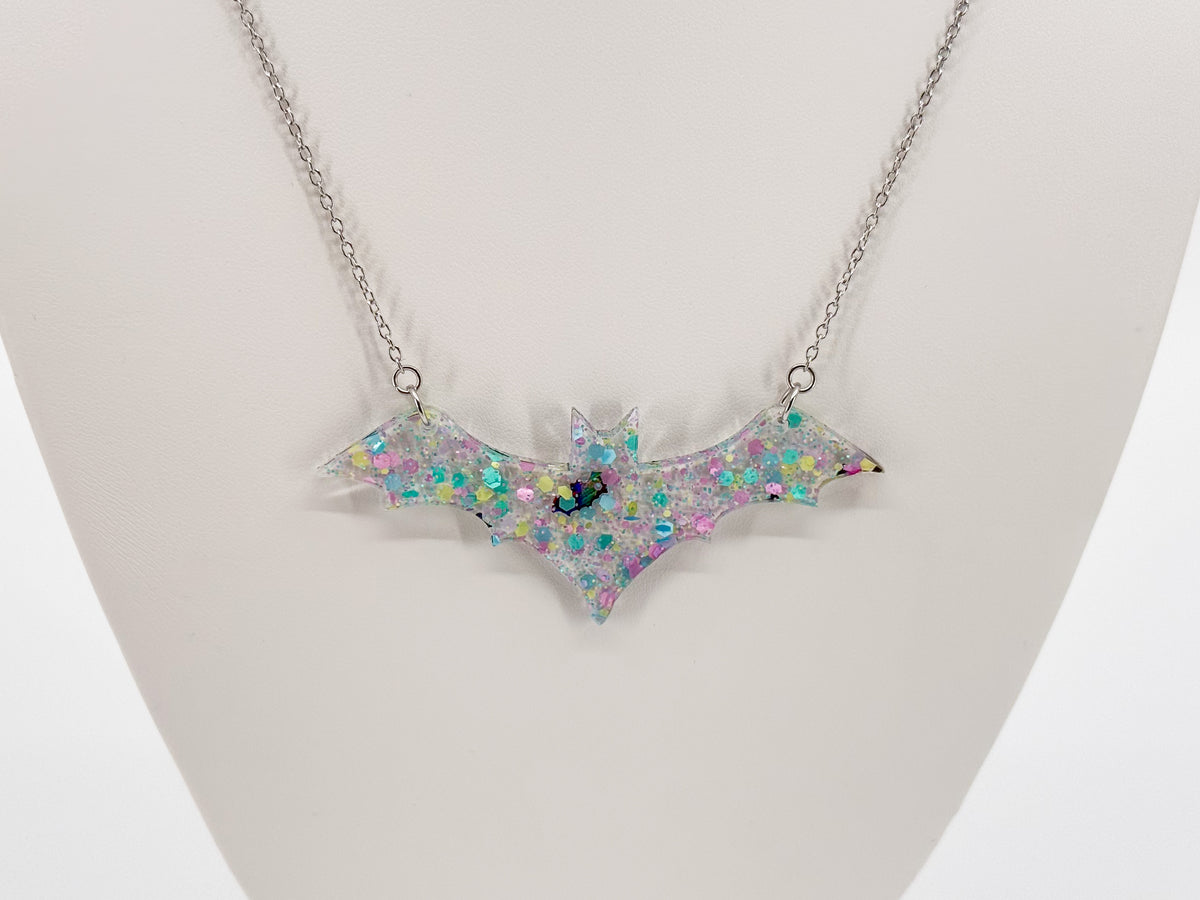 Close-up of a clear bat-shaped pendant filled with pink, yellow and turquoise confetti and small reflective bats.
