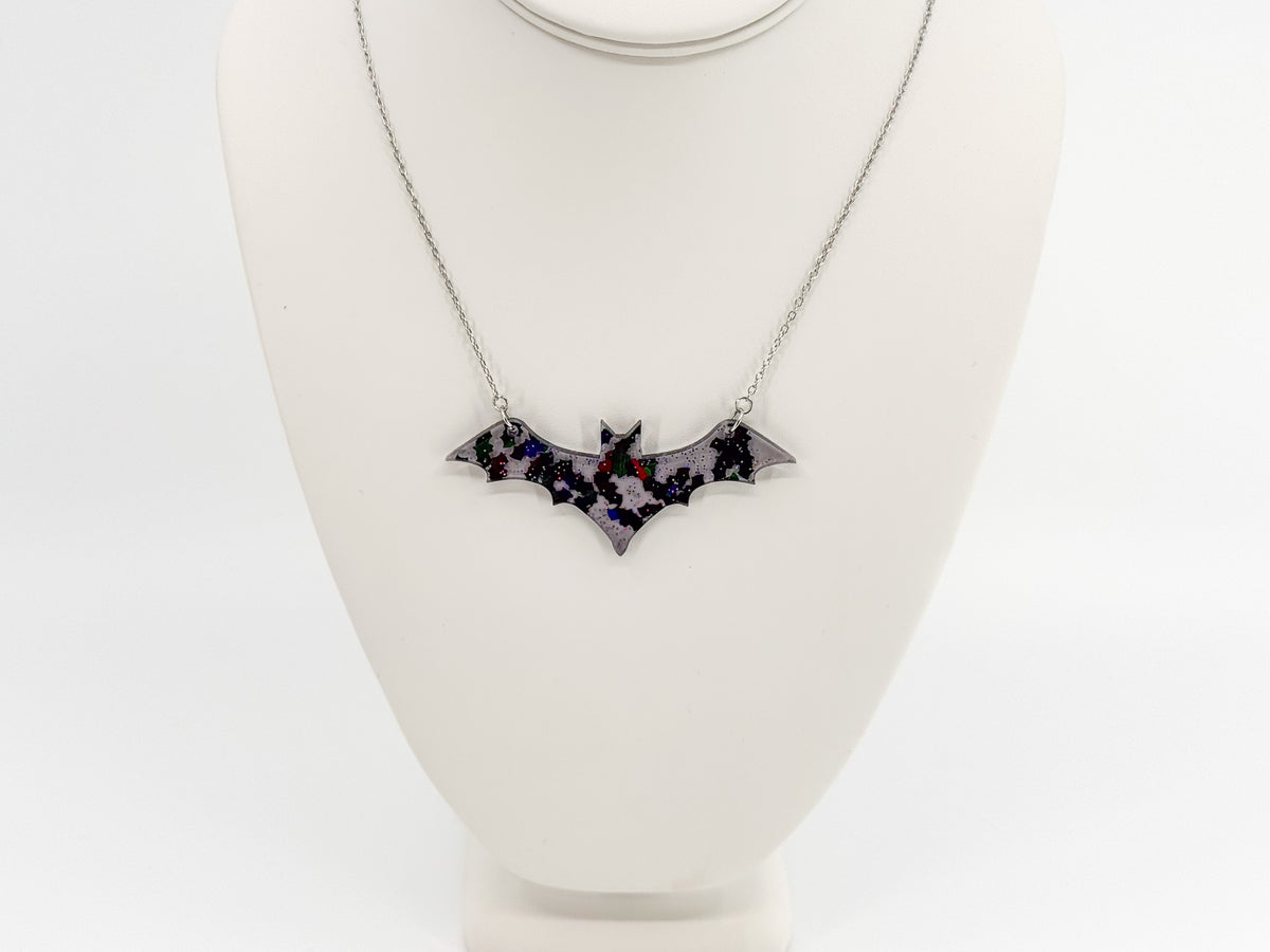 Front view of a smoke gray bat-shaped pendant with reflective bat shapes and a silver-tone chain on a white display bust.
