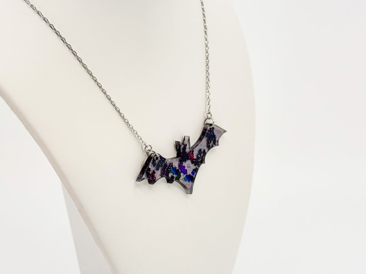 Angled close-up of a smoke gray acrylic bat necklace with reflective iridescent bat shapes on a white display bust.