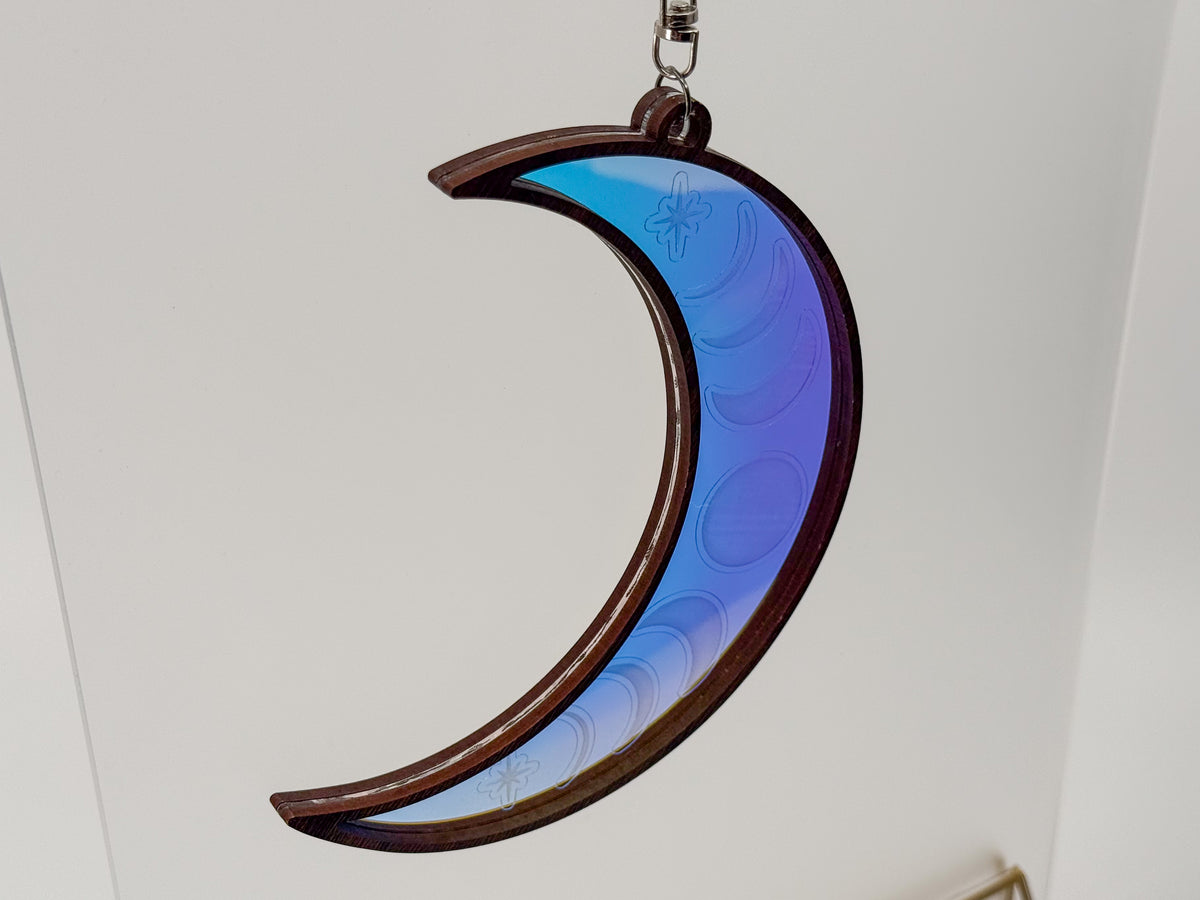 Reverse view of a wood-framed celestial moon suncatcher reflecting blue and purple, with faint moon phase and star engravings.