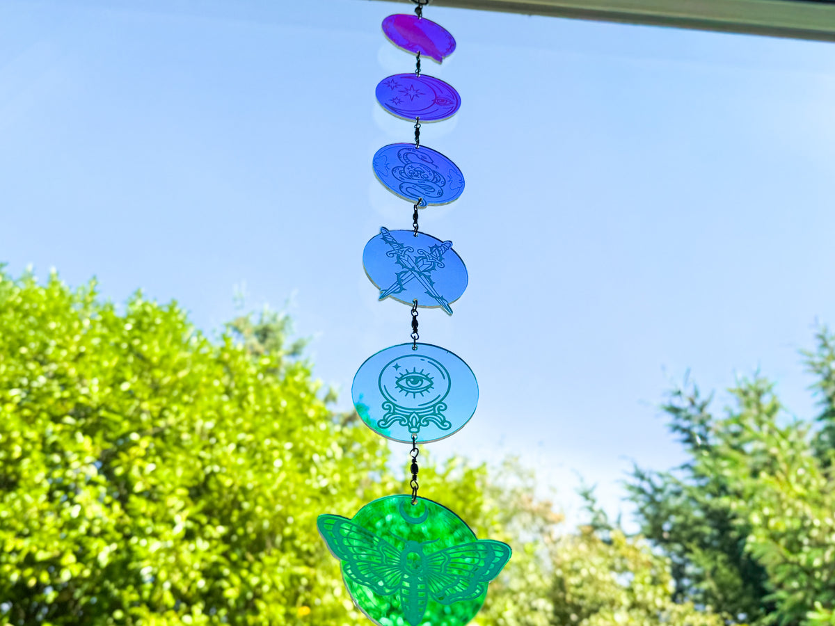 Whimsigothic acrylic mobile glowing purple, blue, and green, with crossed daggers, a crystal ball, and a large moth charm.