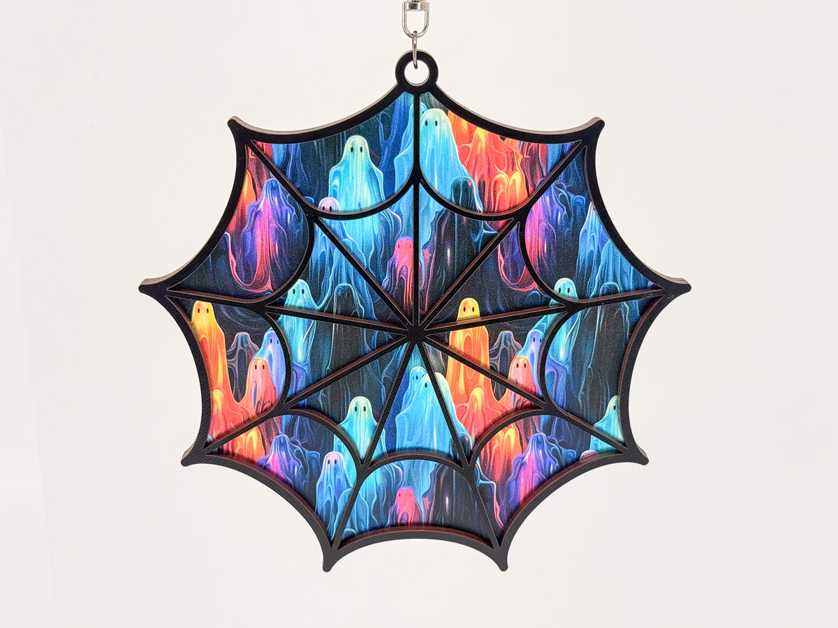 Front view of a black-framed spiderweb suncatcher with blue, turquoise, pink, purple, and orange ghosts on a dark background.