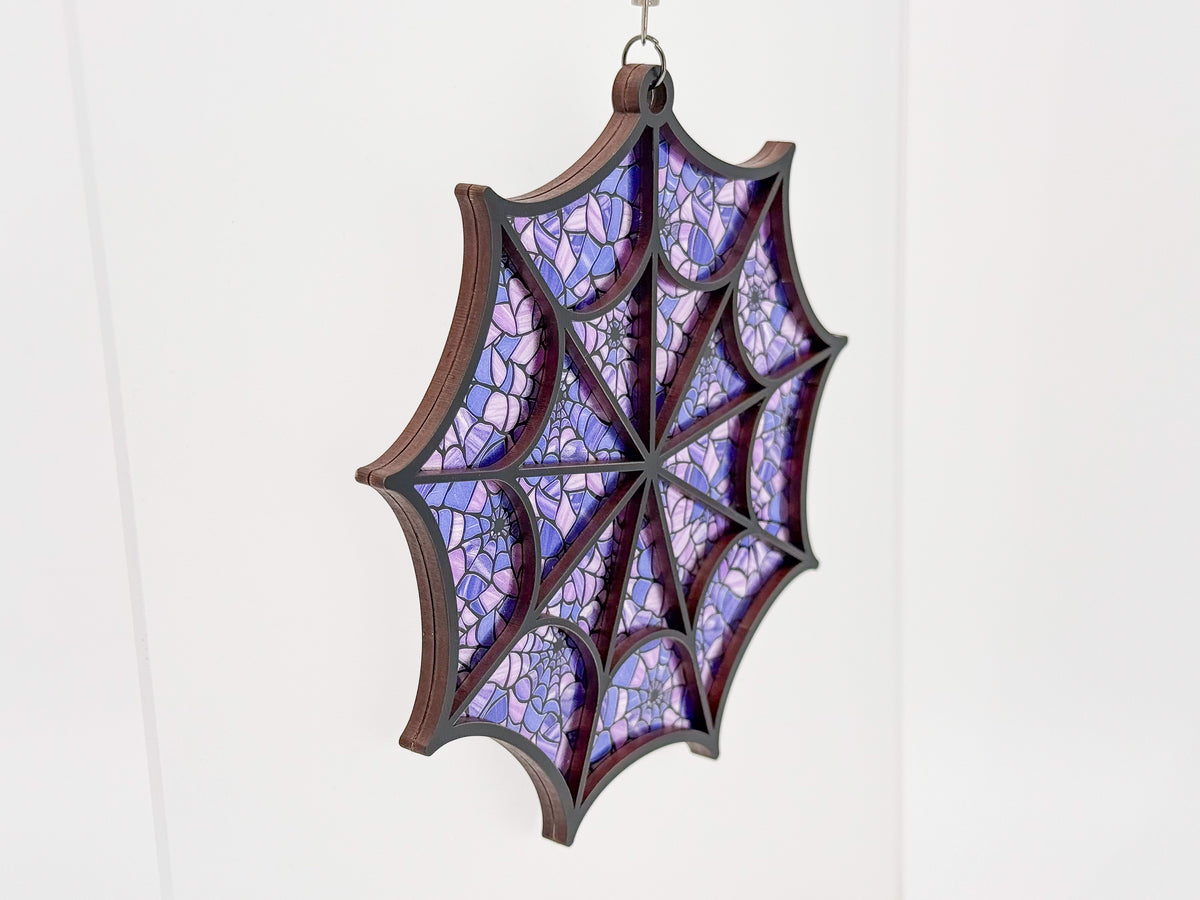 Angled view of the Purple Webs spiderweb suncatcher, showing layered wood edges and a lavender and purple web pattern.