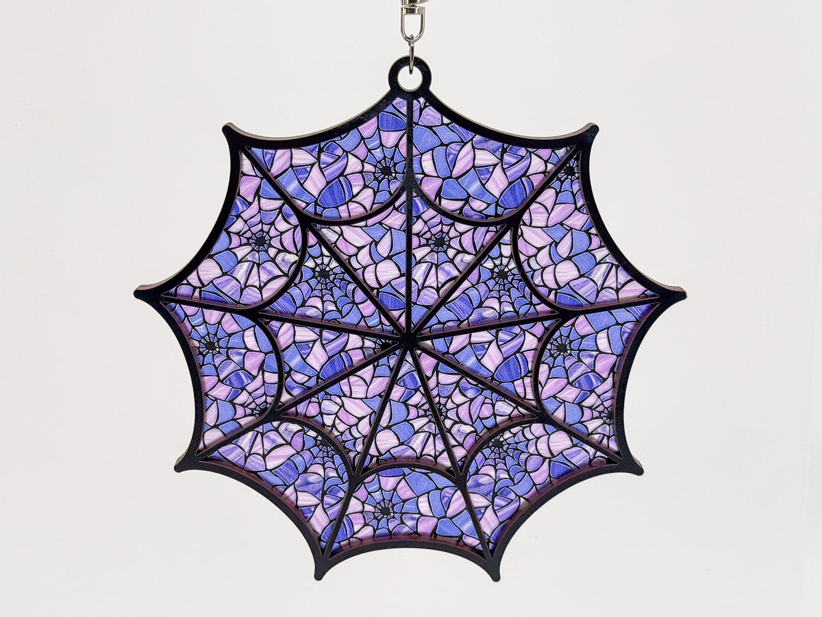 Front view of a black-framed spiderweb suncatcher with a repeating lavender and purple spiderweb pattern.