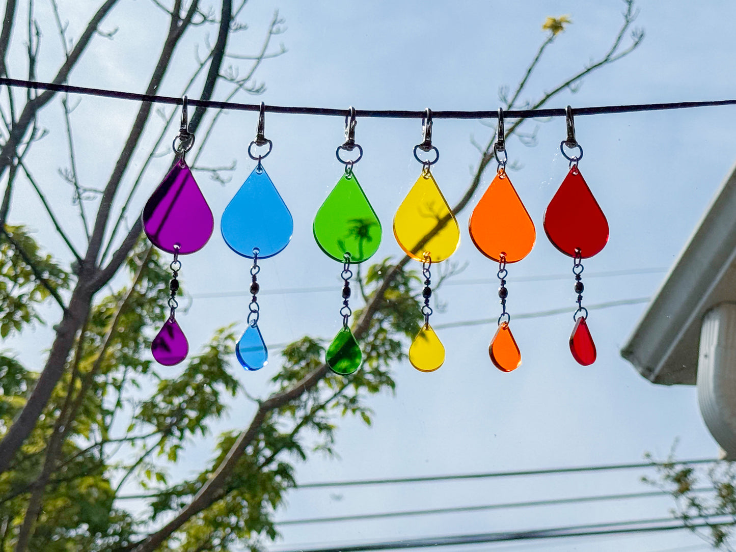 Colorful glass teardrop ornaments hanging on a wire against a blue sky.