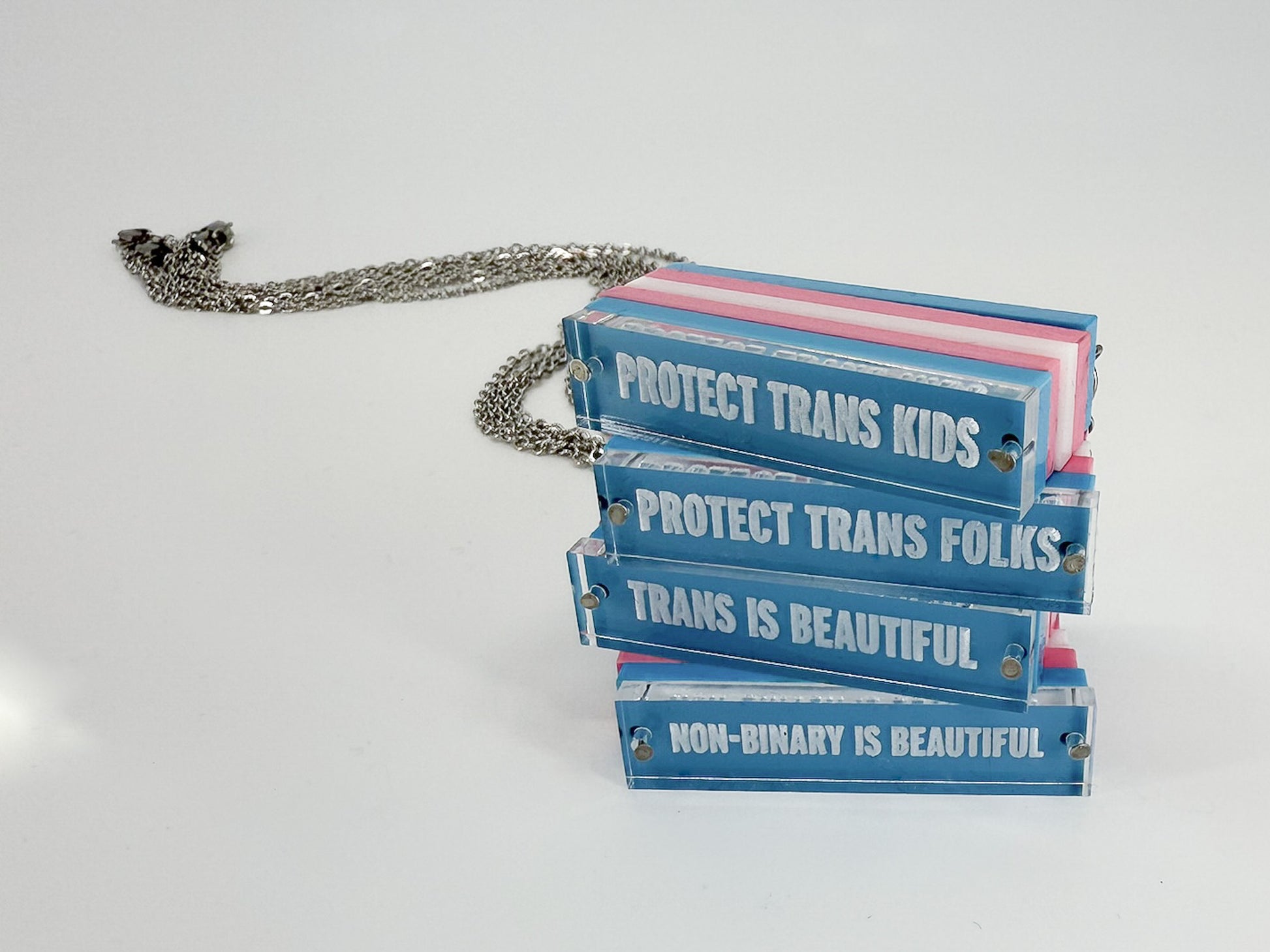 Four necklaces stacked, each reading different phrases: Protect trans kids, Protect trans folks, Trans is beautiful, Non-binary is beautiful