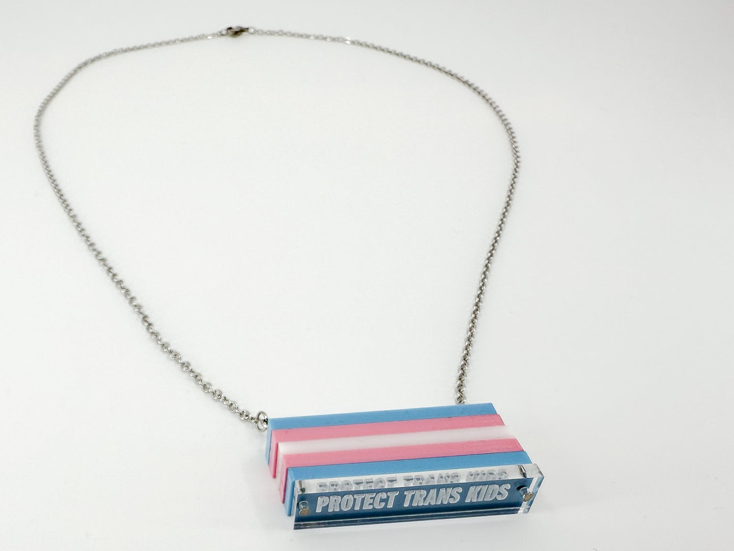 A trans pride flag necklace, with the words "protect trans kids" engraved at the bottom, on a white background.