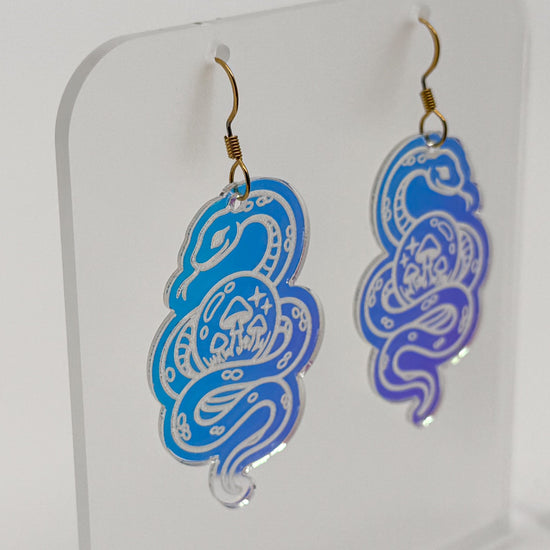 Iridescent snake earrings are displayed on a clear acrylic stand. The stand and earrings are rotating to see all sides.