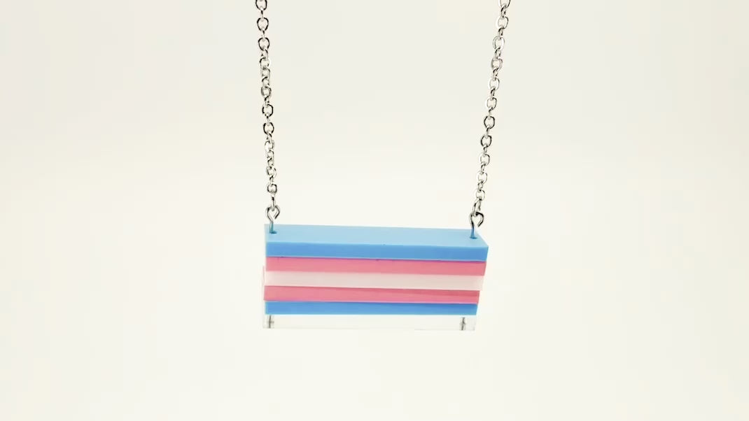 A trans pride flag necklace, shown moving around with a white background.