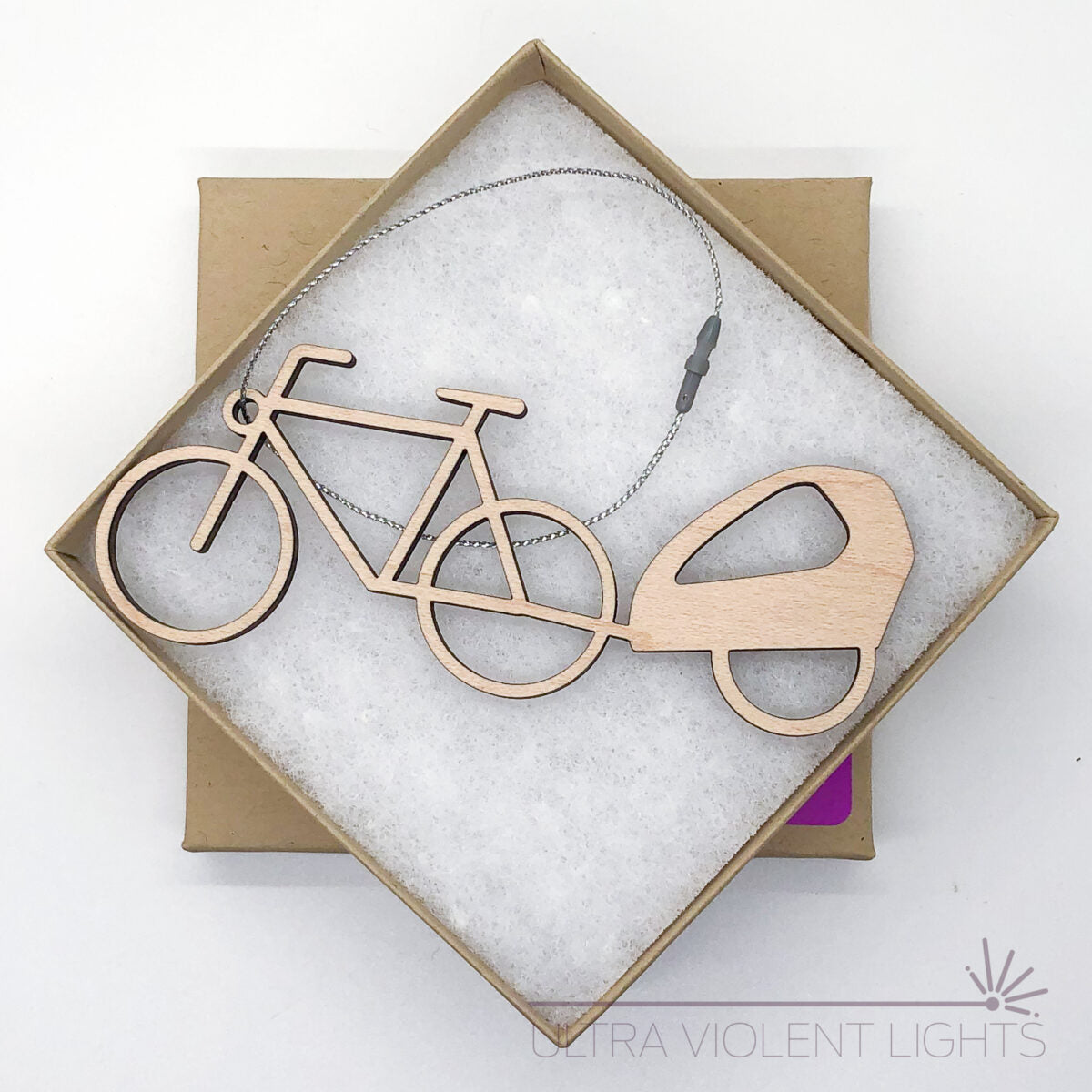 A wooden bike trailer ornament in a square kraft box on a white background