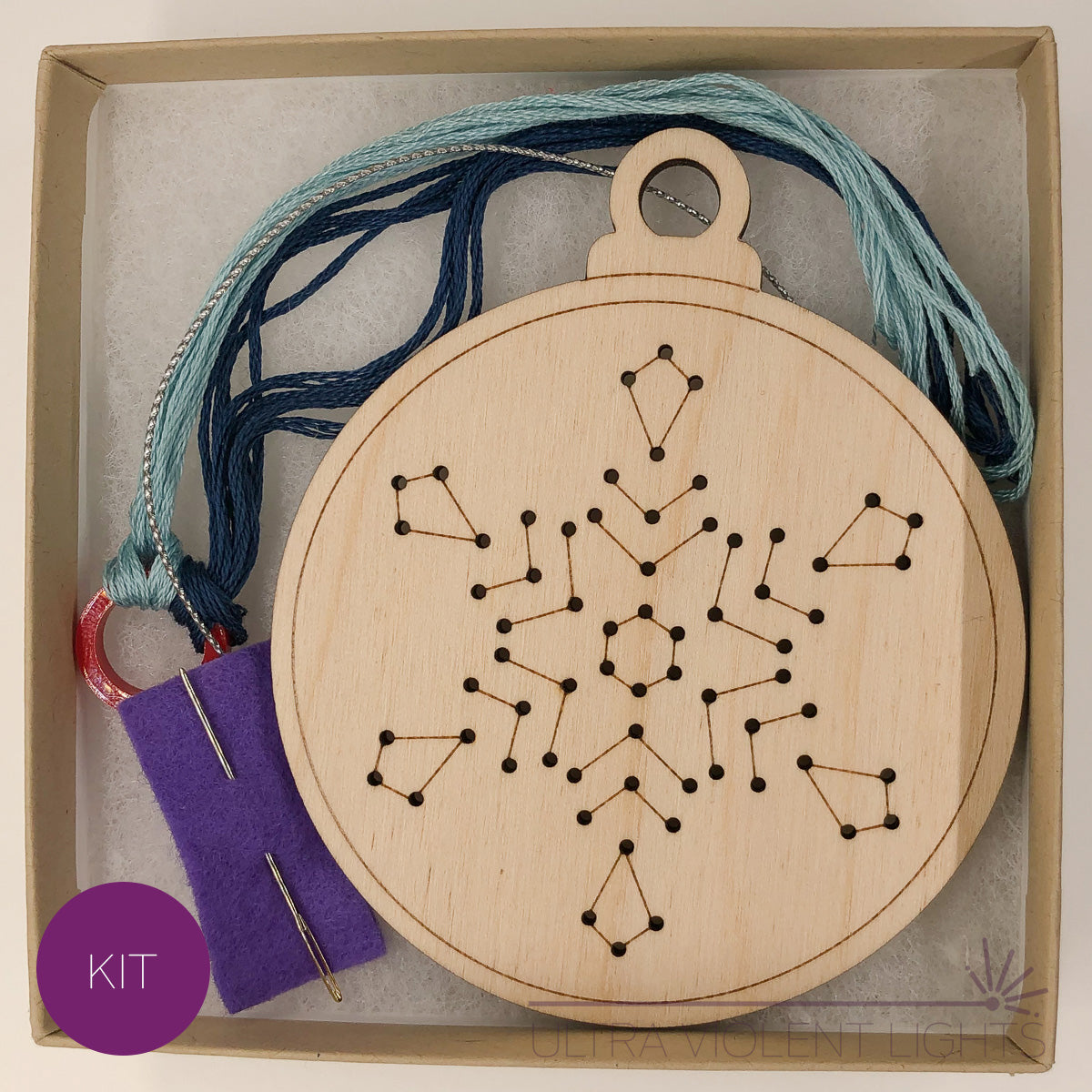 A snowflake wooden embroidery kit with floss and a needle in a box